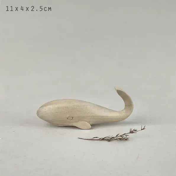 Small light coloured wooden whale figurine on a light gray background with dimensions 11x4x2.5cm.