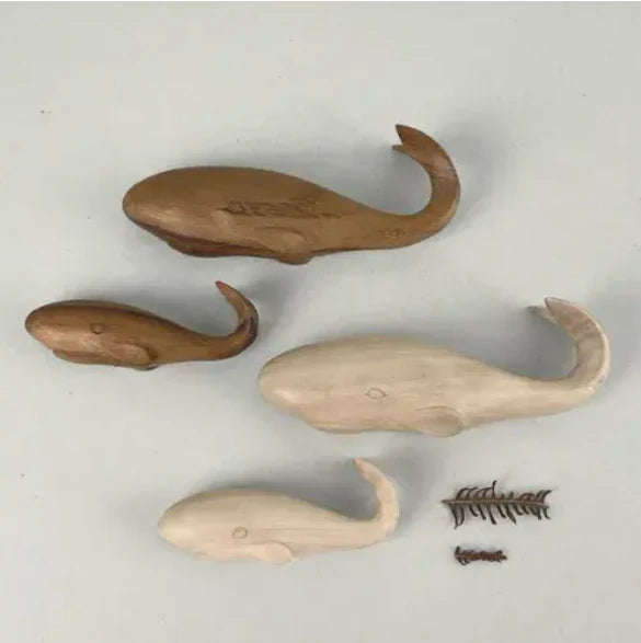 Four wooden whale shaped decorations 2 light and 2 dark wood, with a large and small of each colour, on a light gray background