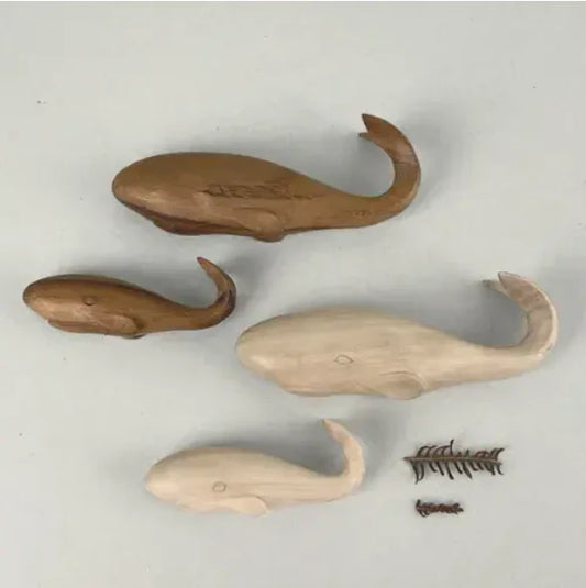 Four wooden whale shaped decorations 2 light and 2 dark wood, with a large and small of each colour, on a light gray background